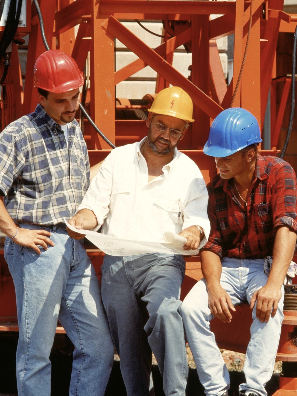 three builders in hard hats reviewing plans on a job site