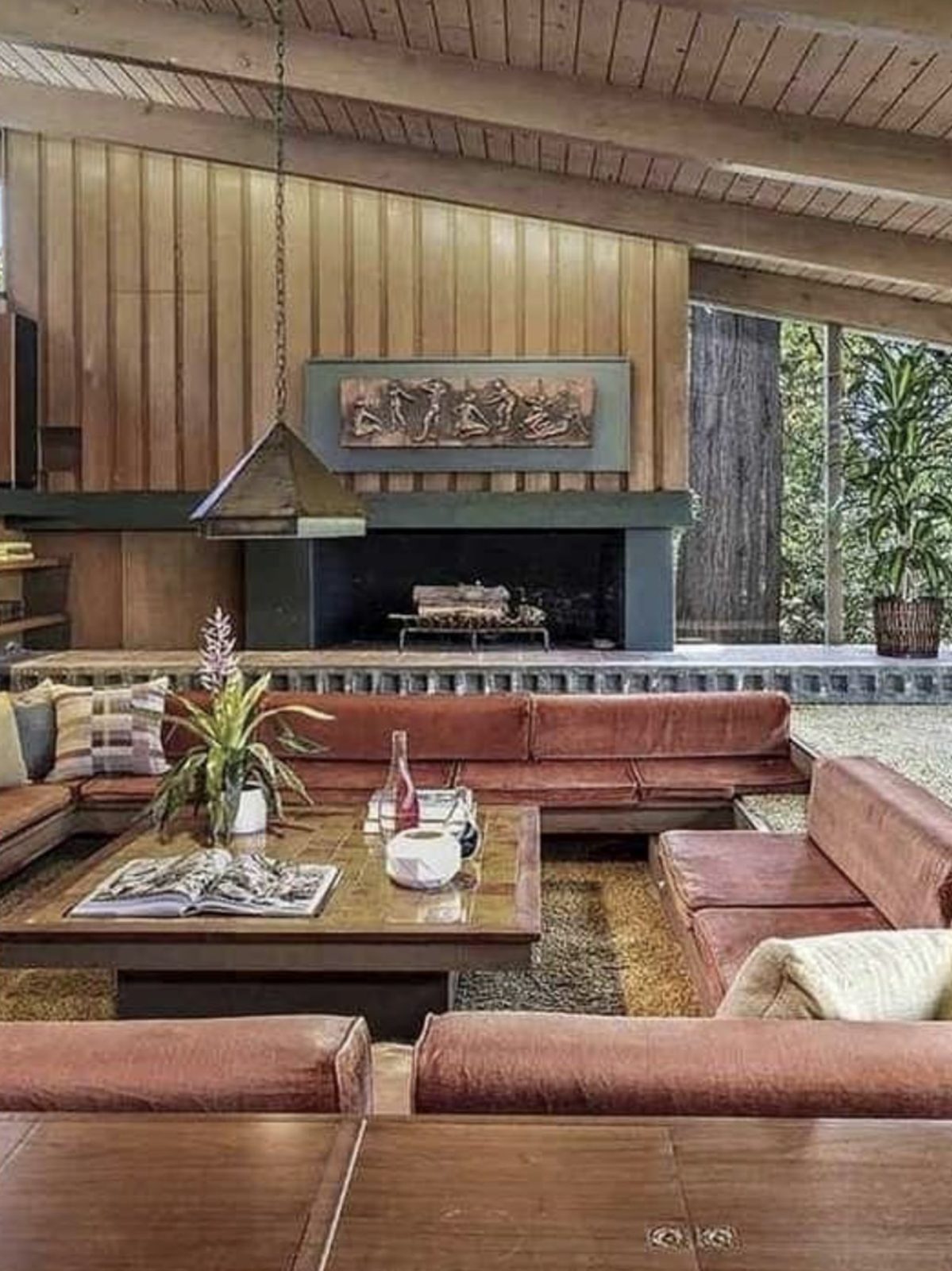 a mid-century sunken living room with wood walls and floor-to-ceiling windows
