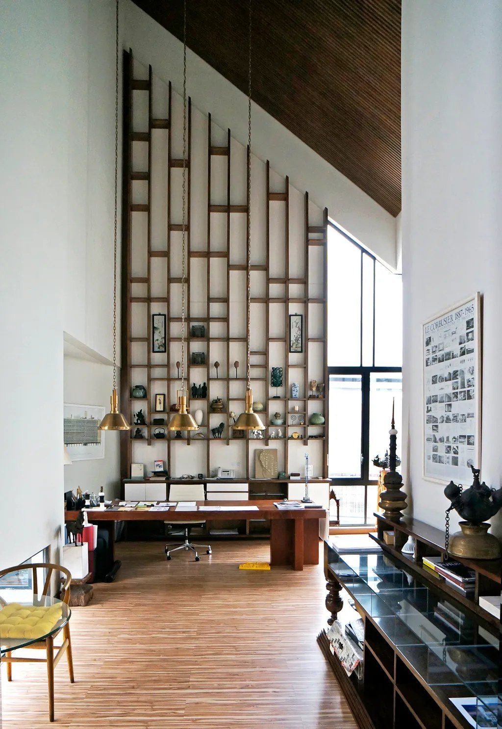 a double-height architecture studio with a wall of wood shelving