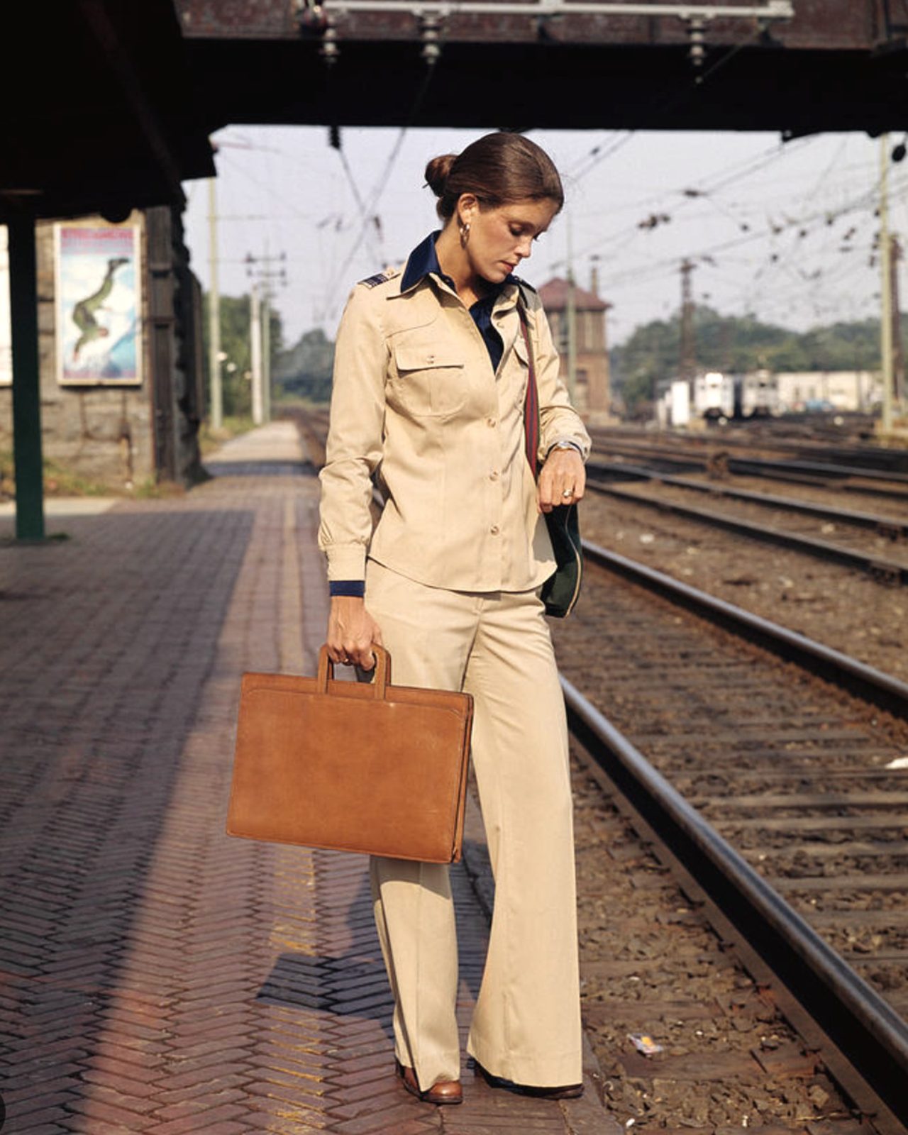 a woman in a tan suit with a leather portfolio checking her watch on a train platform, 1970s