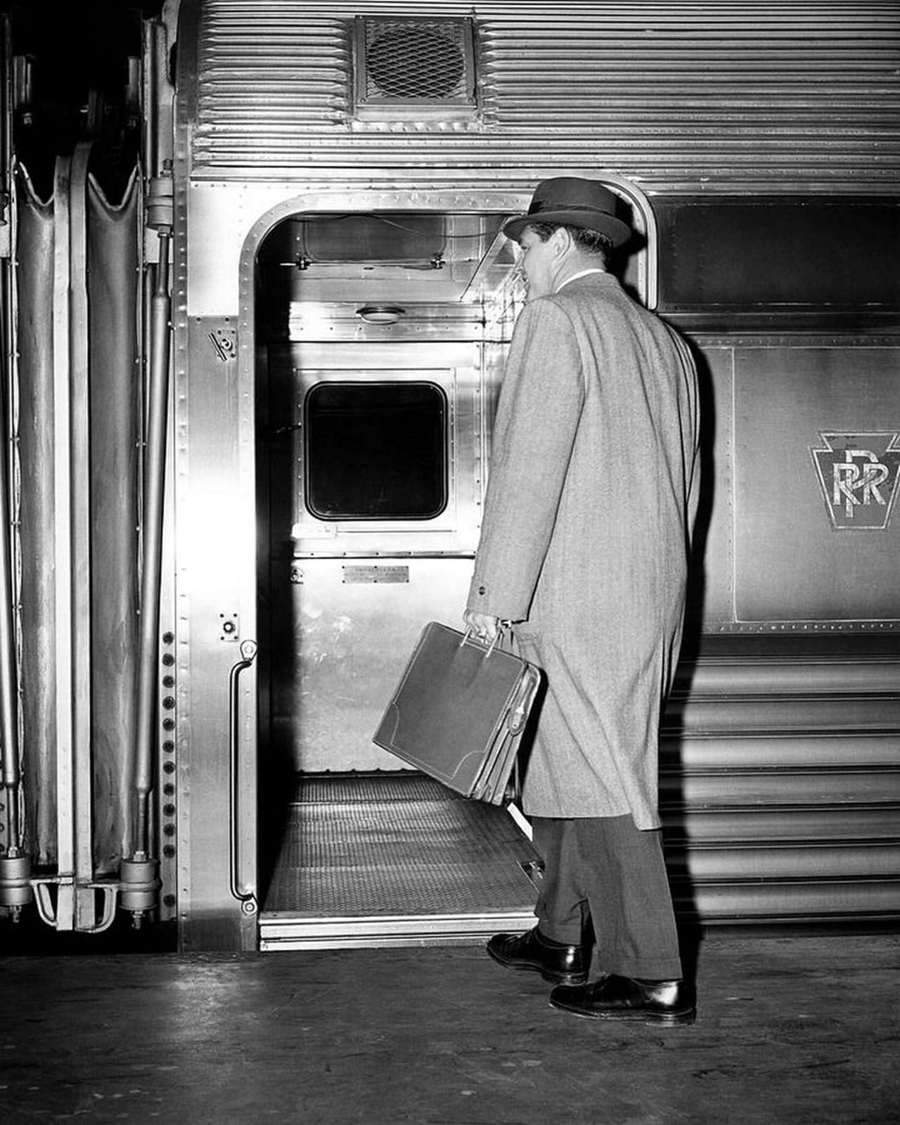 a mid-century businessman in a hat and overcoat, briefcase in hand, boarding a train