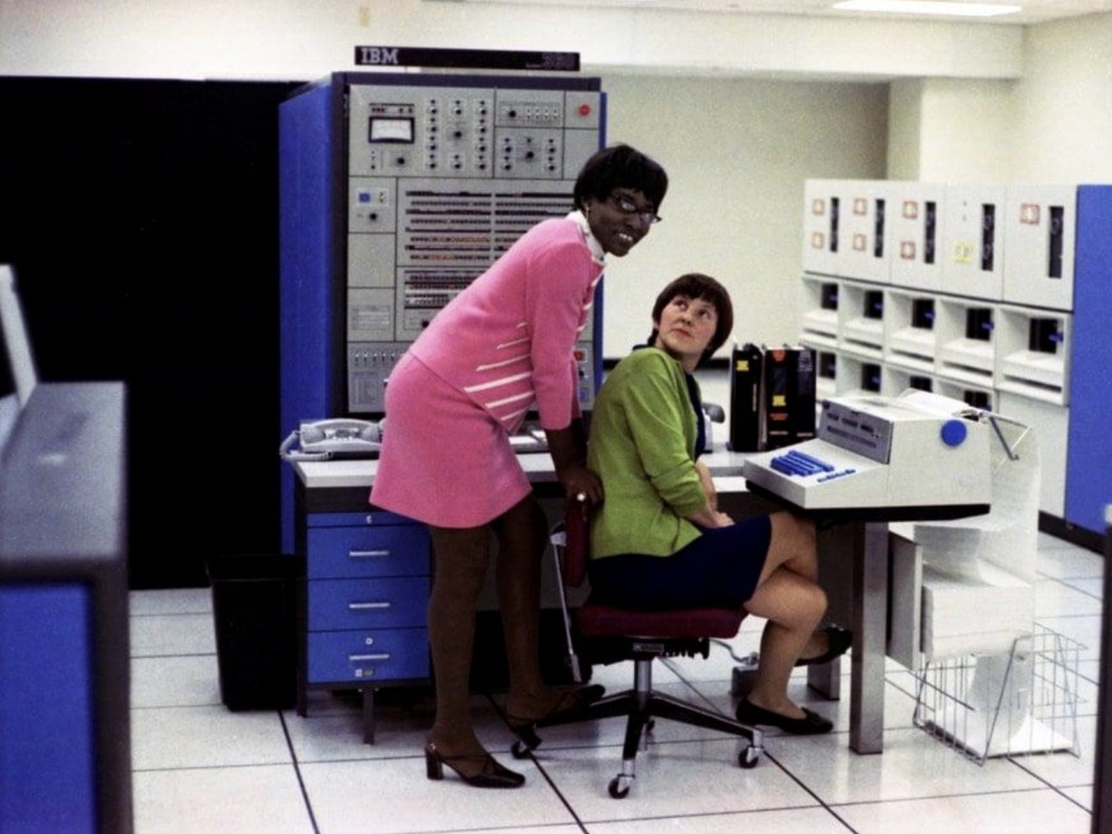 two women in a computer room beside a mainframe console and tape drives, 1970s