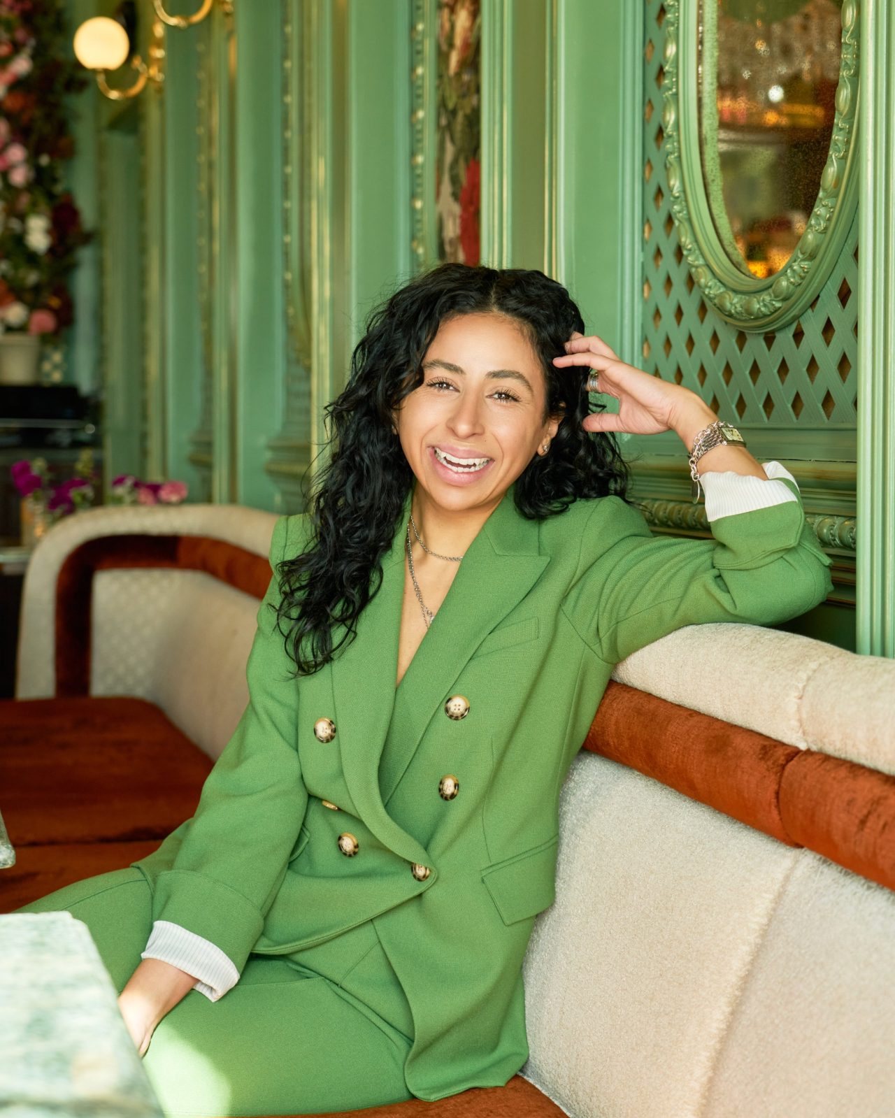 hailey george, founder of hghr, in a green suit, laughing in a cafe banquette
