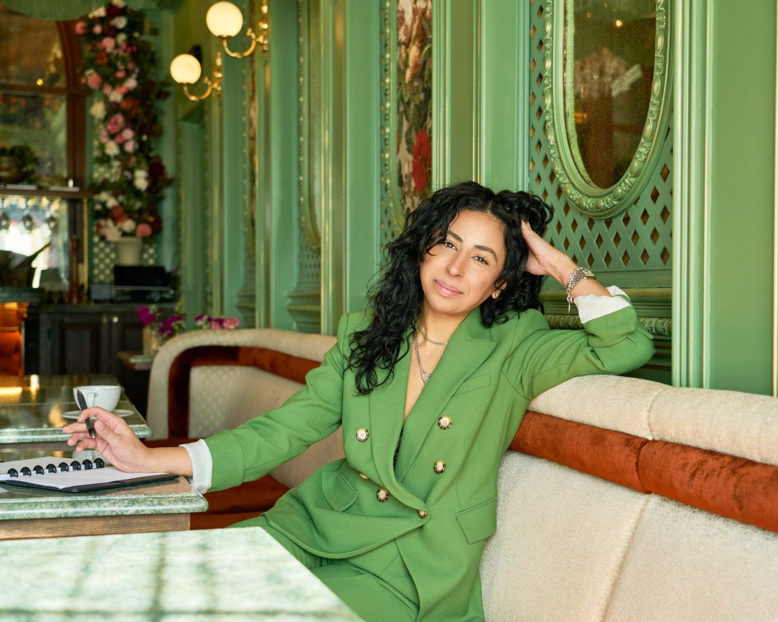 hailey george in a green suit at a cafe banquette, pen in hand