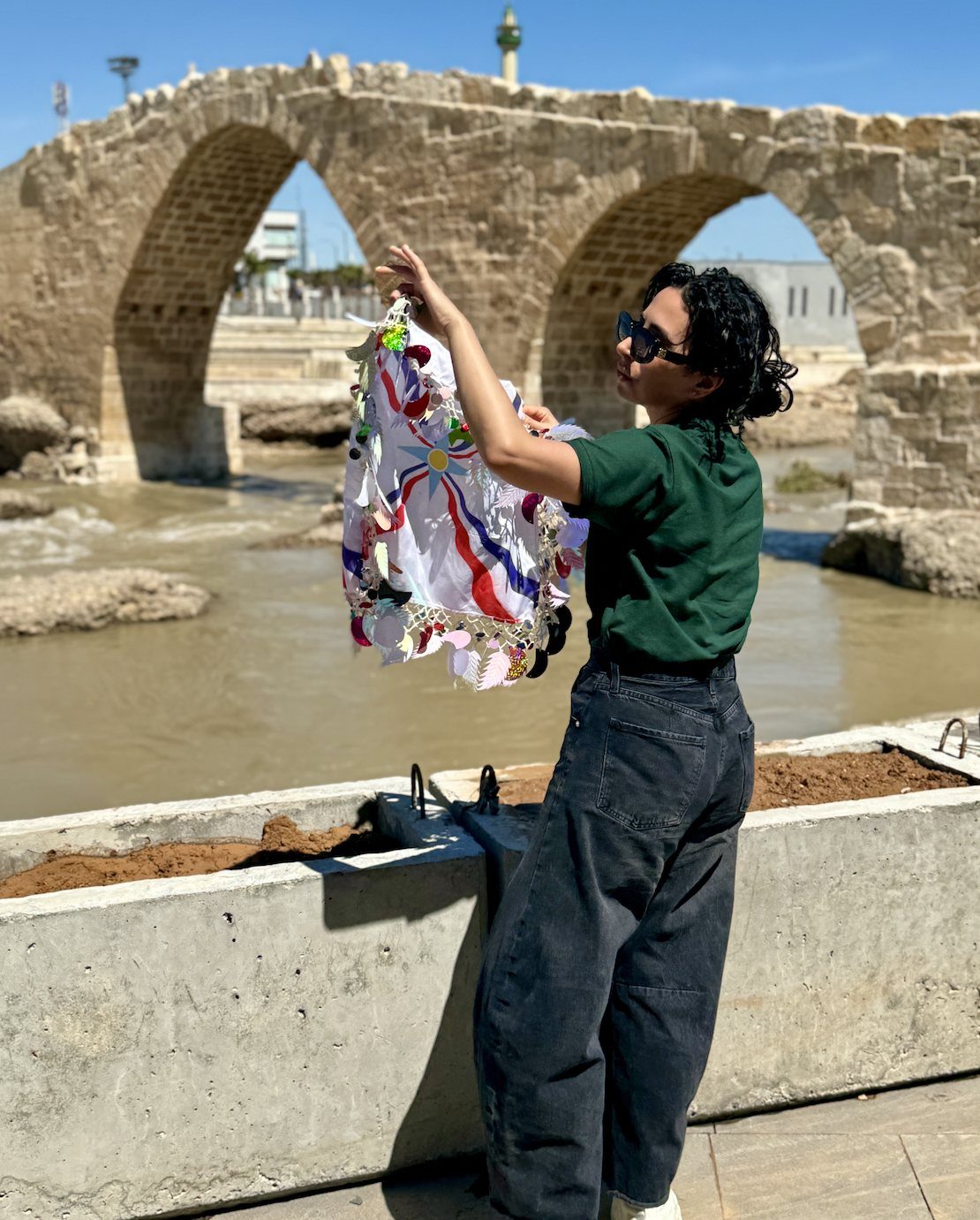hailey holding an assyrian flag in front of an ancient stone bridge in iraq