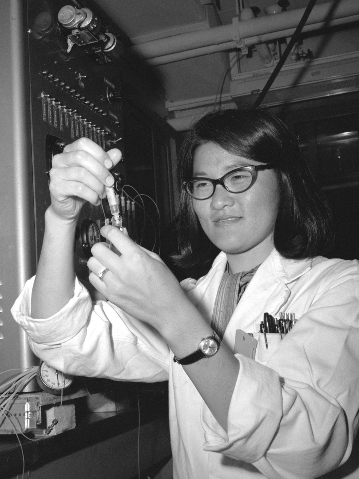 a scientist in a lab coat preparing a sample beside laboratory equipment, 1960s