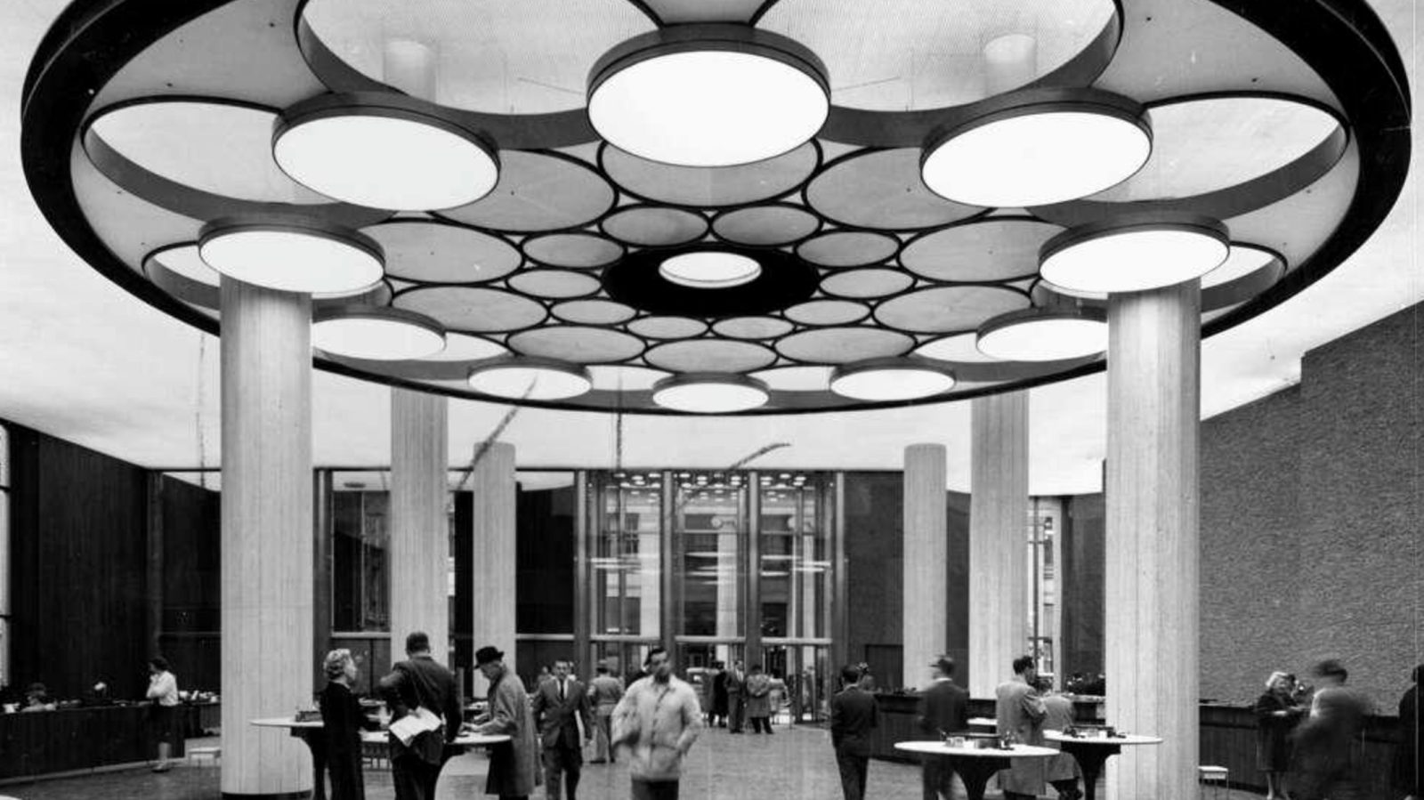 customers at standing tables beneath a circular ceiling of round lights in a wells fargo bank branch, san francisco, 1962