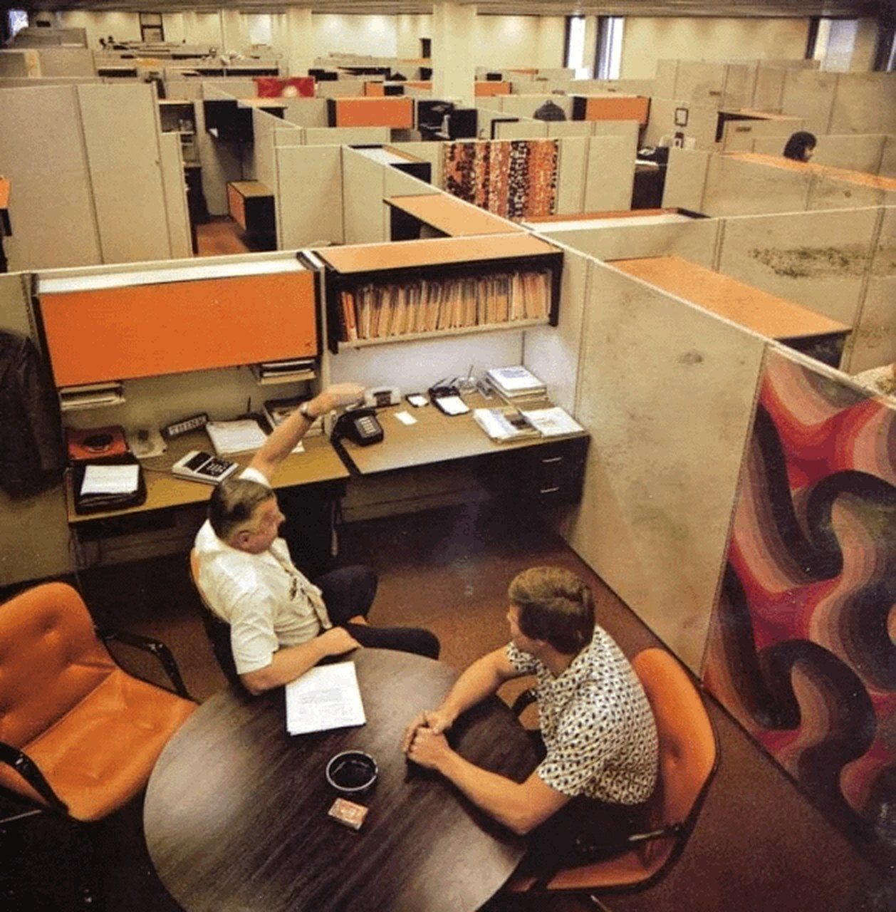 a manager and an employee talking one-on-one at a round table among office cubicles