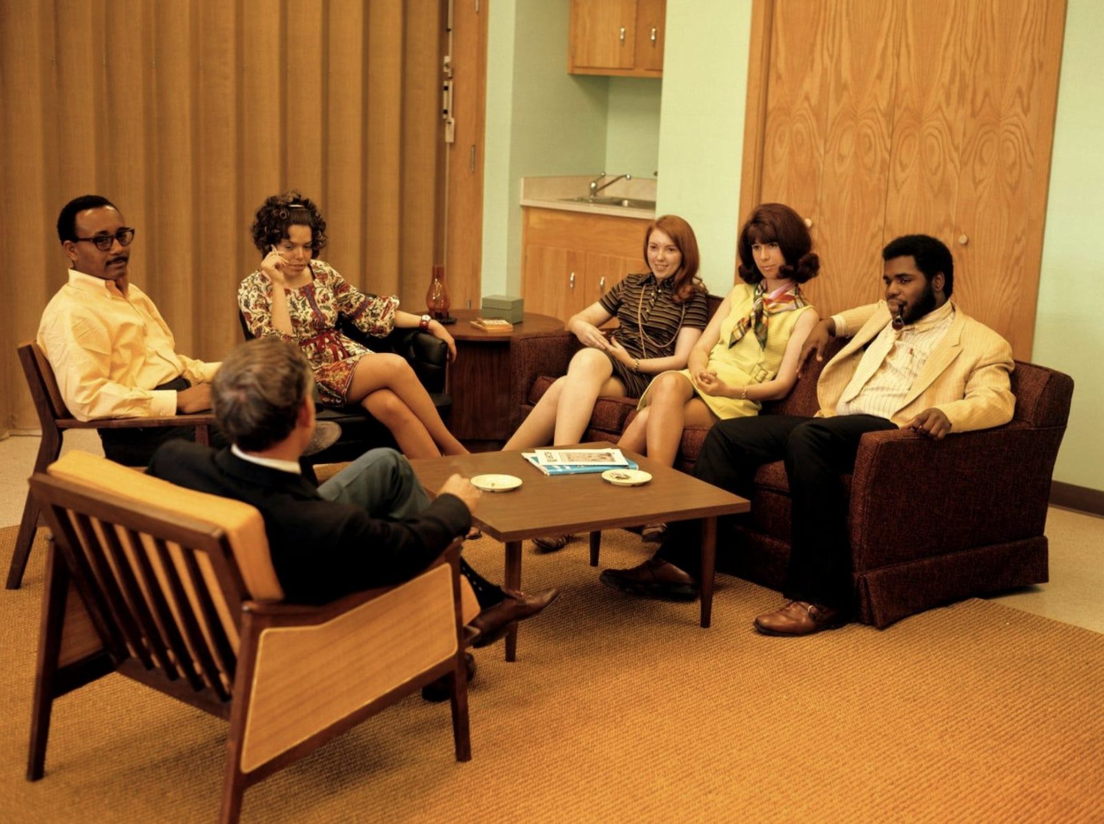 a manager leading a small group discussion in a 1970s lounge