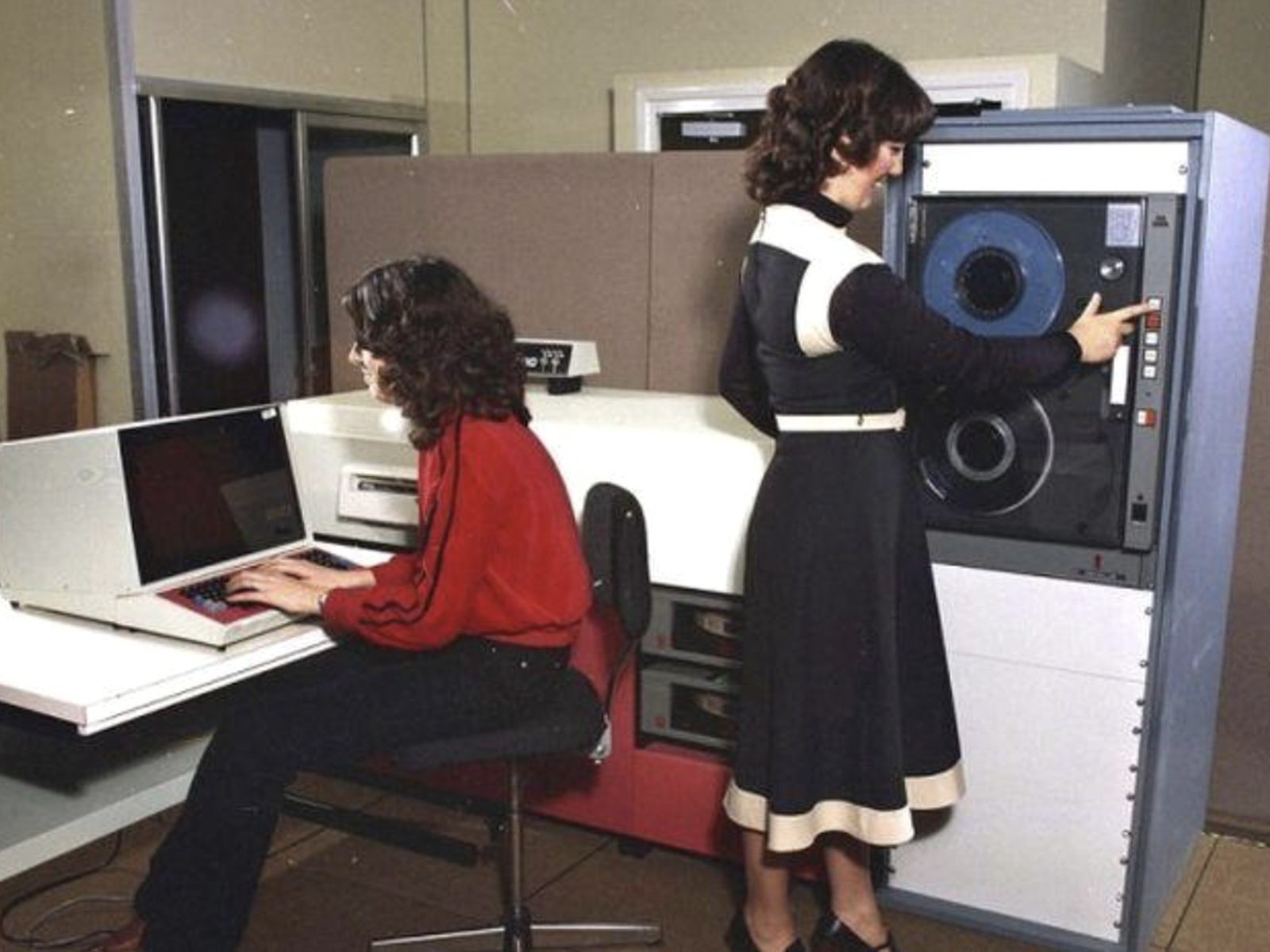 two women running a computer system, one at the keyboard and one at the tape drive, 1970s
